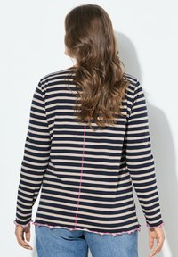 Camiseta de manga larga a rayas en colores azul marino y crema, con un dobladillo ondulado en rosa y costuras a lo largo de la espalda y las mangas.