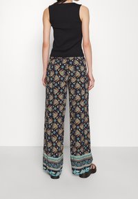 Černý žebrovaný top bez rukávů doplněný námořnickými širokými kalhotami s barevným vzorem paisley a tyrkysovými akcenty na lemu.