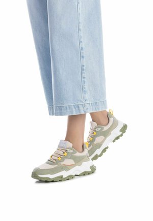 Zapatilla gris claro con acentos verdes, parte superior texturizada, entresuela blanca y suela de goma gruesa. Presenta cordones amarillos y un detalle de marca.