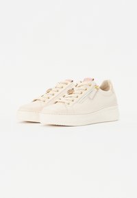 Beiga lädersneakers med guldgripande, texturerade snören och en subtil rosa detalj på tungan; upphöjd sula för extra höjd.