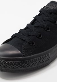 Sneaker nera in tela con superficie texture, punta in gomma, lacci piatti neri e dettagli decorativi sulla suola. Design classico a bassa cima.