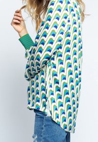 Blusa de satén con un patrón ondulado en verde, azul y blanco. Presenta puños verdes a rayas y un corte holgado. Bajo con diseño deconstruido.