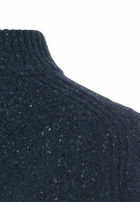 Pull à col roulé tricoté bleu foncé avec col côtelé et texture tachetée sur fond uni.