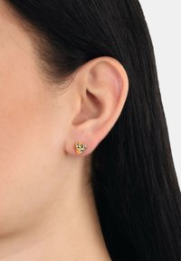 Orecchini a bottone in oro a forma di anelli intrecciati, con una finitura lucida e piccoli accenti neri. Indossati sul lobo dell'orecchio.