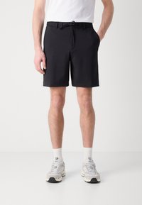 Pantaloni scurți negri texturați cu talie cu șnur, buzunare laterale și o croială adaptată, purtați cu șosete atletice albe și adidași.