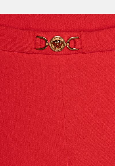Red fabric with a smooth texture, featuring a gold embellishment and chain detail at the waist. Clean lines and no visible patterns.