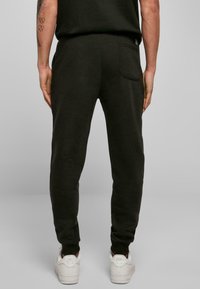 Mørkegrønne sweatpants i blødt fleece-materiale med en enkelt baglomme og tapered ben, parret med hvide sneakers.