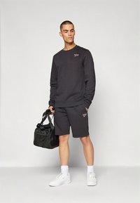 Conjunto de sweatshirt de algodão cinza escuro e calções, tecido misto de algodão, detalhe de logótipo no peito, combinado com ténis brancos e uma bolsa de desporto preta.