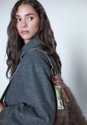 Grauer Strickmantel mit weitem Kragen, kombiniert mit einer Handtasche aus Kunstfell und dekorativen Schlüsselanhängern in Grün und Braun.