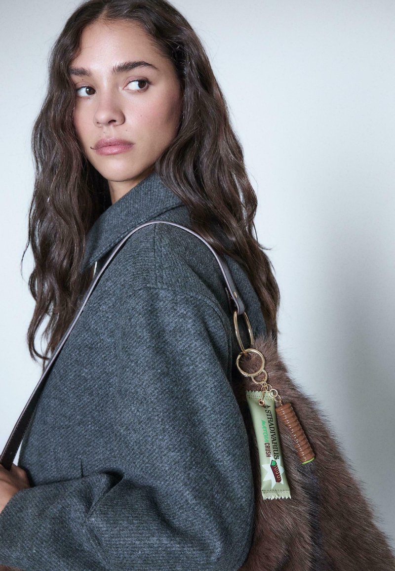 Cappotto lavorato a maglia grigio con ampio colletto, abbinato a una borsa con pelliccia sintetica e dettagli decorativi di portachiavi in verde e marrone.