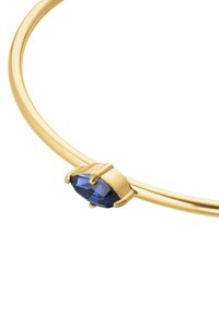 Brazalete de metal dorado con una gema azul en forma de marquesa sujeta por un engaste de cuatro garras. Acabado de superficie suave y pulido.