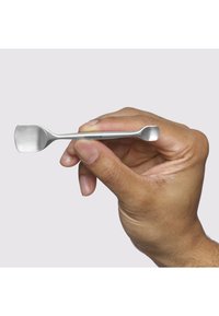 Mano che tiene un piccolo spingicuticole in acciaio inossidabile a doppia estremità con punte piatte e angolate su uno sfondo uniforme.