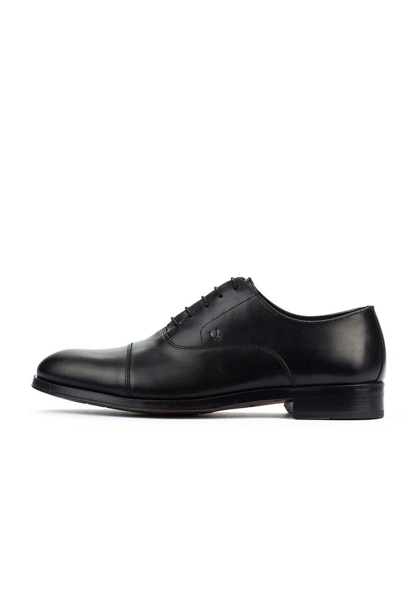 Zapato de vestir Oxford para hombre de cuero negro con cordones cerrados, puntera cap y tacón bajo apilado sobre un fondo blanco.