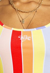 Pestrý pruhovaný top bez rukávů z žebrované látky, s červenými, žlutými, oranžovými a fialovými pruhy. Obsahuje bílé logo Nike a vrstvené řetězce.