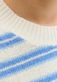 Gros plan sur un col côtelé d'un pull crème avec des rayures diagonales bleu clair et bleu moyen.