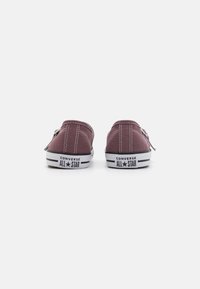 Scarpe slip-on in tela bordeaux con suole in gomma bianche. Presentano cuciture bianche e il marchio "CONVERSE ALL STAR" sul tallone. Design piatto.