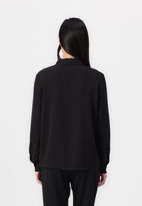 Blusa nera a maniche lunghe con colletto, texture liscia e vestibilità comoda. Presenta polsini aderenti e orlo dritto sul fondo.