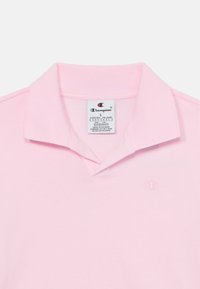 Svetloružová polo košeľa z bavlny, s klasickým golierom, krátkymi rukávmi a vyšitou logom na ľavej hrudi. Nálepka je viditeľná.