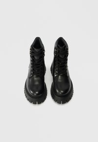 Μαύρες δερμάτινες μπότες αστραγάλου με λείο φινίρισμα, στρογγυλή μύτη, παχύ χοντρό πάτο και κορδόνια. Ασημένια αξεσουάρ στις τρυπίτσες των κορδονιών.