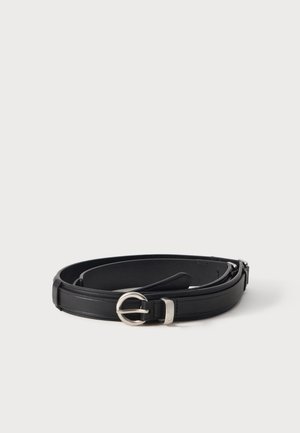 Ceinture en cuir noir avec une boucle ronde argentée, enroulée sur une surface blanche.