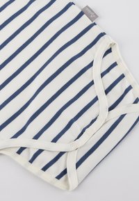 Weißer Stoffbodies mit navyblauen Streifen; besitzt Druckknopfverschlüsse und weiche Kanten; aus Baumwolle mit glatter Textur.
