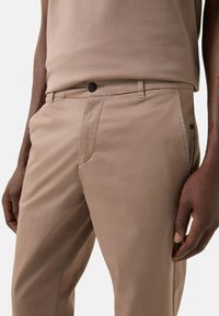 Beige, slanke bukser i glat stof med knappelukning og sidelommer. Designet er minimalistisk med rene linjer.