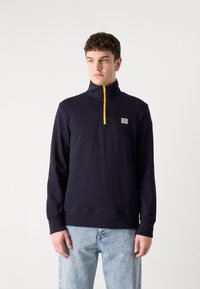 Hanorac navy cu fermoar pe jumătate, fabricat din bumbac, cu un fermoar galben, manșete ribbate și un mic patch cu logo pe partea stângă a pieptului.