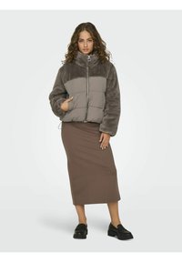 Faux fur and padded bomber jacket in gray and taupe with a high collar, zip closure, side pockets, and worn over a brown midi skirt.