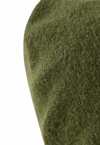 Close-up van gestructureerde olijfgroene wollen stof met een patroonweving, waarop zachte plooien en een licht fuzzy oppervlakte zichtbaar zijn.