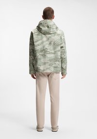 Ελαφρύ μπουφάν με κουκούλα σε πράσινο και κρεμ με αφηρημένο σχέδιο, με μακριά μανίκια, φαρδιά γραμμή και ίσιο κάτω μέρος. Διαφορετική υφή υφάσματος.