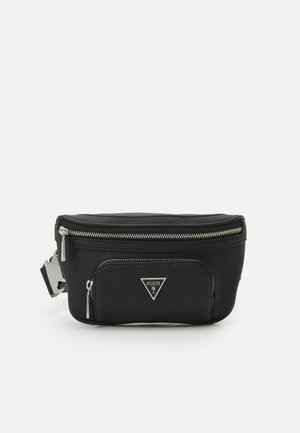 Schwarze Guess-Gürteltasche mit zwei Reißverschlussfächern und einem dreieckigen Metalllogo auf der Vordertasche vor einfarbigem Hintergrund.