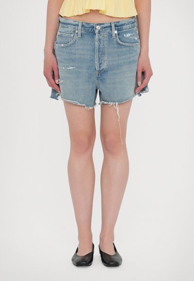 Pantaloni shorts in denim di colore azzurro chiaro con orlo sfrangiato, dettagli strappati e design tradizionale a cinque tasche, abbinati a scarpe nere di tipo flat.