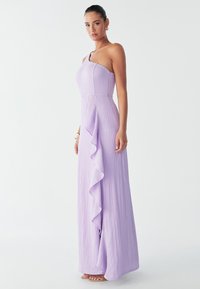 Lila yhdelle olalle suunniteltu mekko, jossa on teksturoitu kangas, tiukka paita ja sivuilla laskeutuva röyhelöyksityiskohta, maahan ulottuva malli.