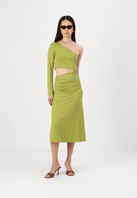 Aszimmetrikus, két részes ruha élénk zöld színben, hosszú ujjú cropped top és egy testhez simuló midi szoknya oldalsó kivágással.