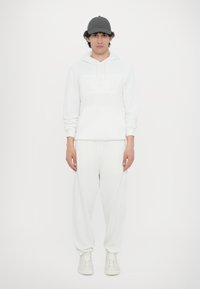 Hvid hættetrøje med prægede logo, parret med matchende hvide joggers. Har en frontlomme og ribbede manchetter. Grå caps fuldender looket.