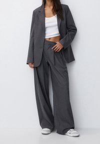 Costume gris à fines rayures composé d'un blazer ajusté et d'un pantalon à jambes larges. Porte sur un crop top blanc et accompagné de baskets blanches.