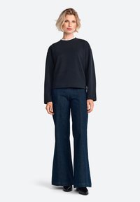 Zwart sweatshirt met ronde hals, gecombineerd met wijde donkere spijkerbroek. Gladde textuur, ontspannen pasvorm en contrasterende kraagdetail.