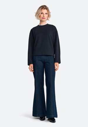 Černá mikina s kulatým výstřihem, doplněná rozšířenými tmavě džínovými kalhotami. Hladká textura, volný střih a kontrastní detail límce.