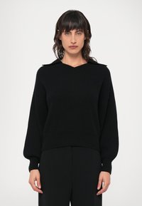 Fekete kötött pulóver V-nyakkal és galléros kialakítással. Laza ujjak és bordázott textúra jellemzi, testre szabott fekete nadrággal párosítva.