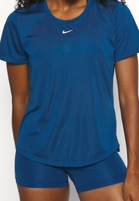 Nainen, jolla on päällään yhteensopiva sininen urheilun lyhythihainen paita ja tiukat shortsit, joissa rinnassa on valkoinen Nike-logo.