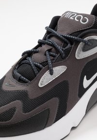 Černá a šedá teniska z materiálů síťoviny a semiše, s obloukovým designem, reflexními prvky a bílým logem Nike na boku.