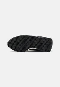 Semelle de chaussure noire avec un motif en caoutchouc texturé, présentant une forme incurvée et des bords renforcés. Semelle plate pour une meilleure traction et stabilité.