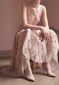 Vestido maxi con bordado floral en rosa suave, que presenta un corsé ajustado, falda con volantes y una superposición transparente. Complementado con tacones altos nude.