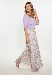 Lila lange mouw top, met geplooide mouwen, gecombineerd met een bloemenpatroon, vloeiende maxi rok in zachte pasteltinten. Zilveren sleehakken.