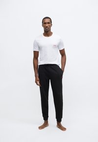 Biele tričko s okrúhlym výstrihom a malým červeným logom "HUGO", doplnené čiernymi teplákmi s podobným logom. Jemná textúra a pohodlný strih.