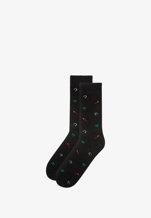 Black socks featuring a pattern of red chili peppers, green shamrocks, and silver horseshoes. Smooth texture and standard crew shape.