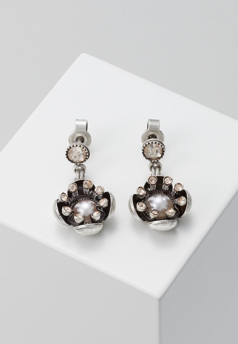 Paire de boucles d'oreilles pendantes en argent avec des cristaux ronds et des centres façon perle dans un design floral, exposée sur une surface blanche.