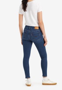 Jeans ajustados azul con cintura alta, tejido de mezclilla y dos bolsillos traseros. Combinados con una camiseta blanca y zapatillas beige.