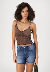 Top court smocké marron avec des bords froncés, associé à un short en denim bleu avec un ourlet effiloché et des poches. La texture est douce et décontractée.