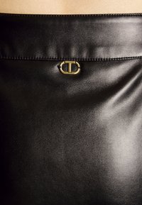 Sac en cuir noir avec un fermoir logo Twinset doré près du centre en haut, montrant une surface lisse et légèrement texturée.